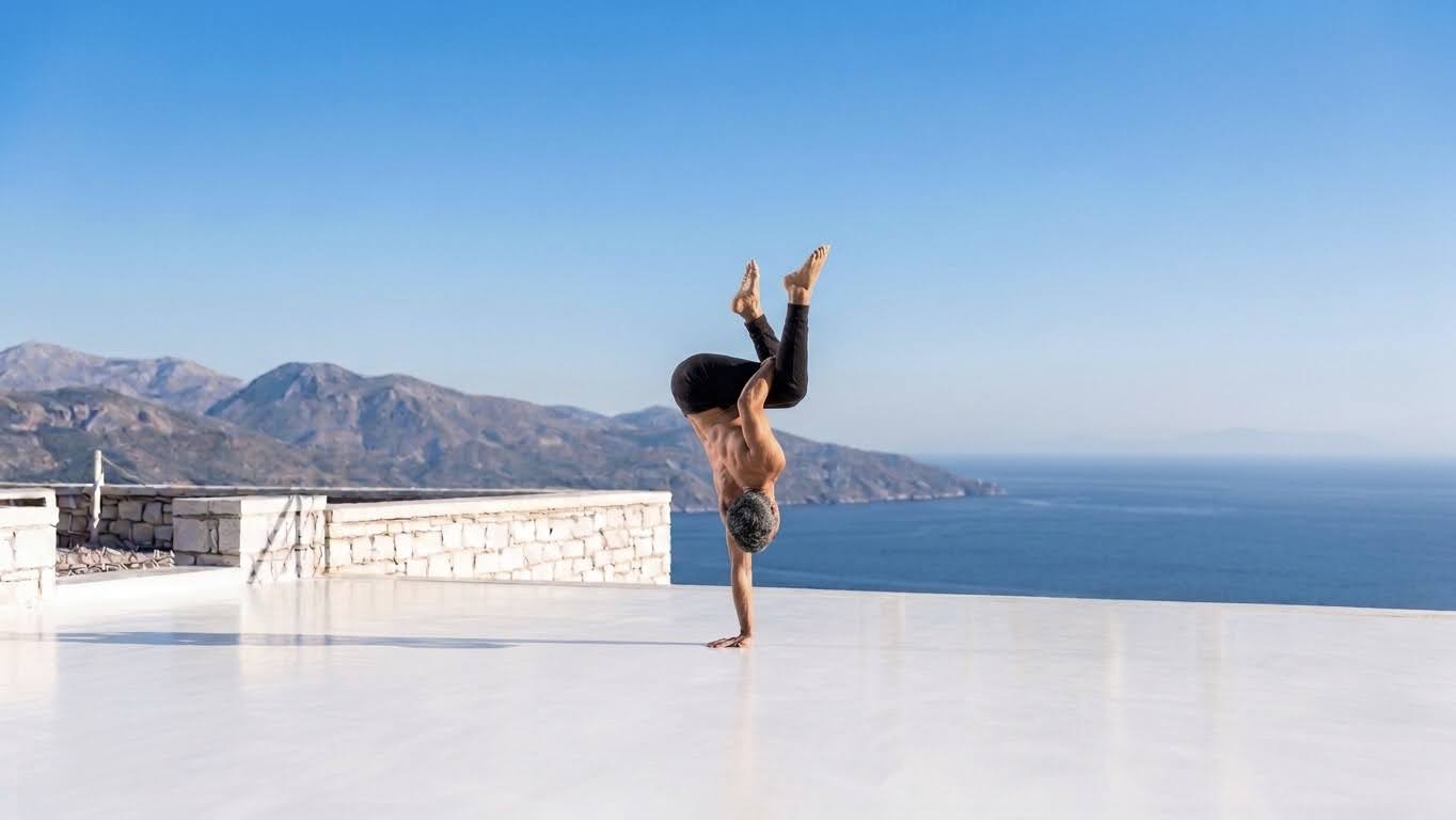 Yuval Oz in a one-arm handstand on a white terrace with the Mediterranean sea in the background