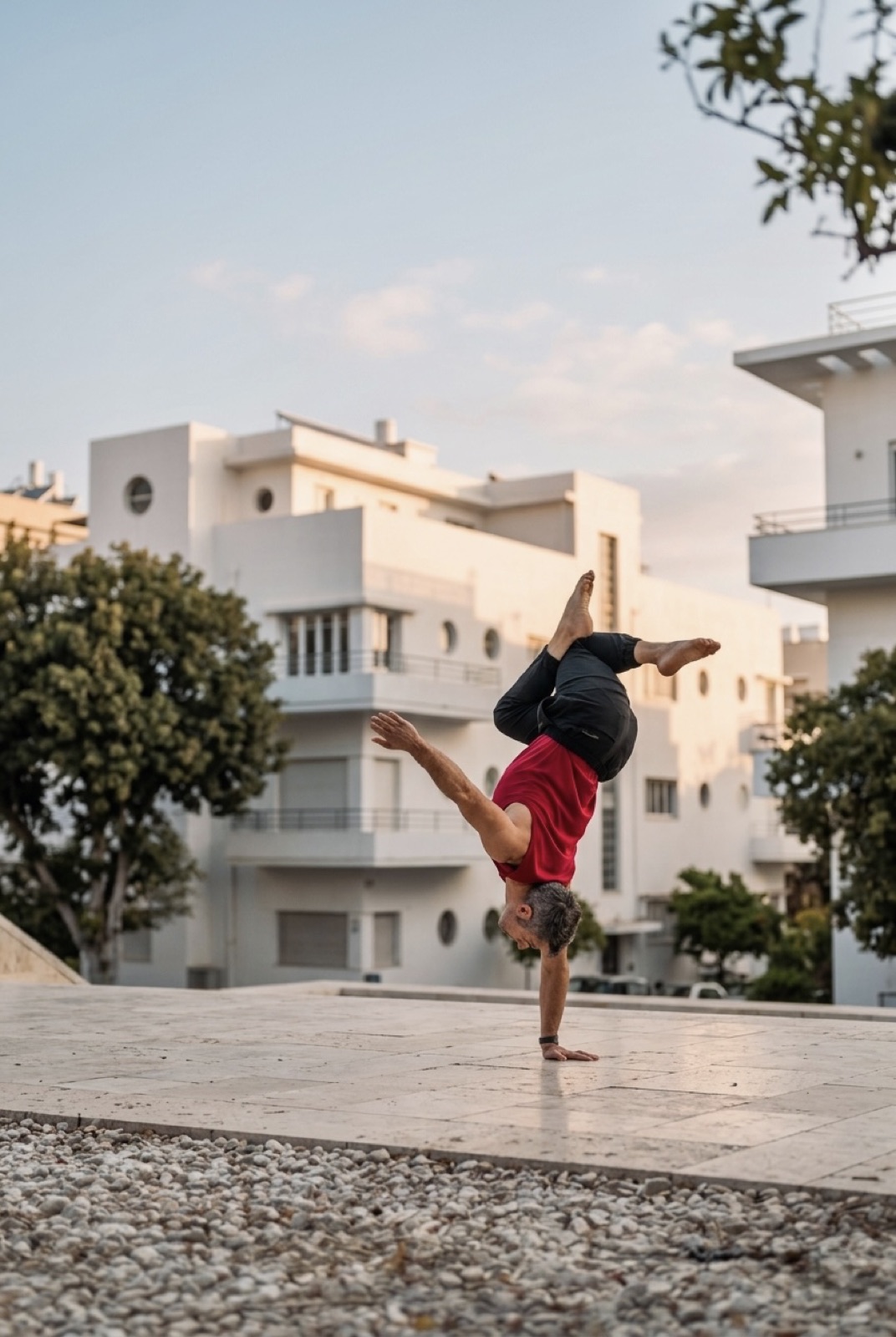 Yuval Oz performing a one-arm handstand in Tel Aviv with Bauhaus architecture in the background